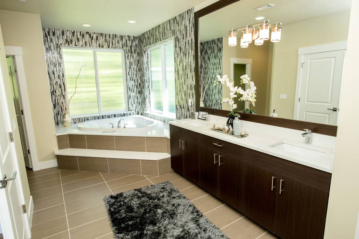 A dark gray shag bath rug on a beige tile floor in front of a long dark wood double vanity with a large mirror