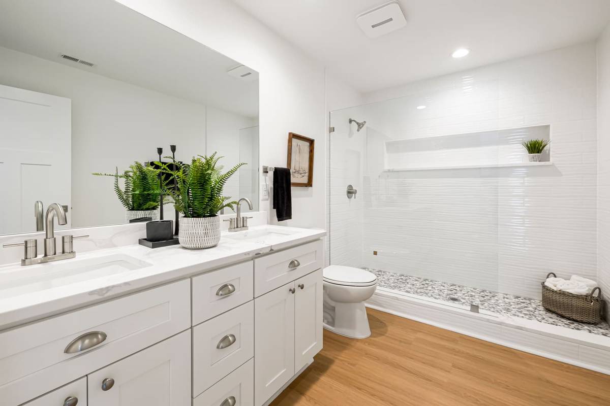 A white bathroom with a square exhaust fan and a recessed light in the ceiling above a glass walk-in shower