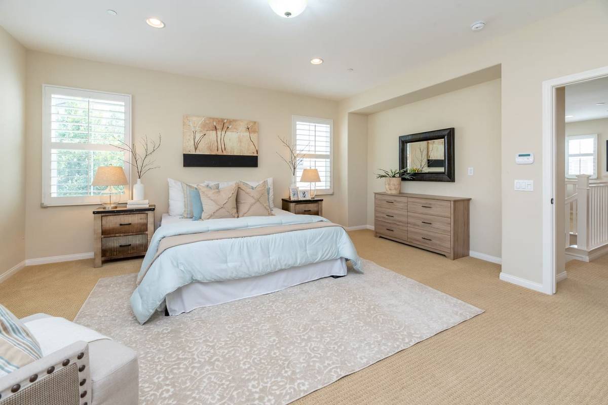 A bedroom with a light blue comforter on the bed, wood nightstands with lamps on both sides and a wide dresser