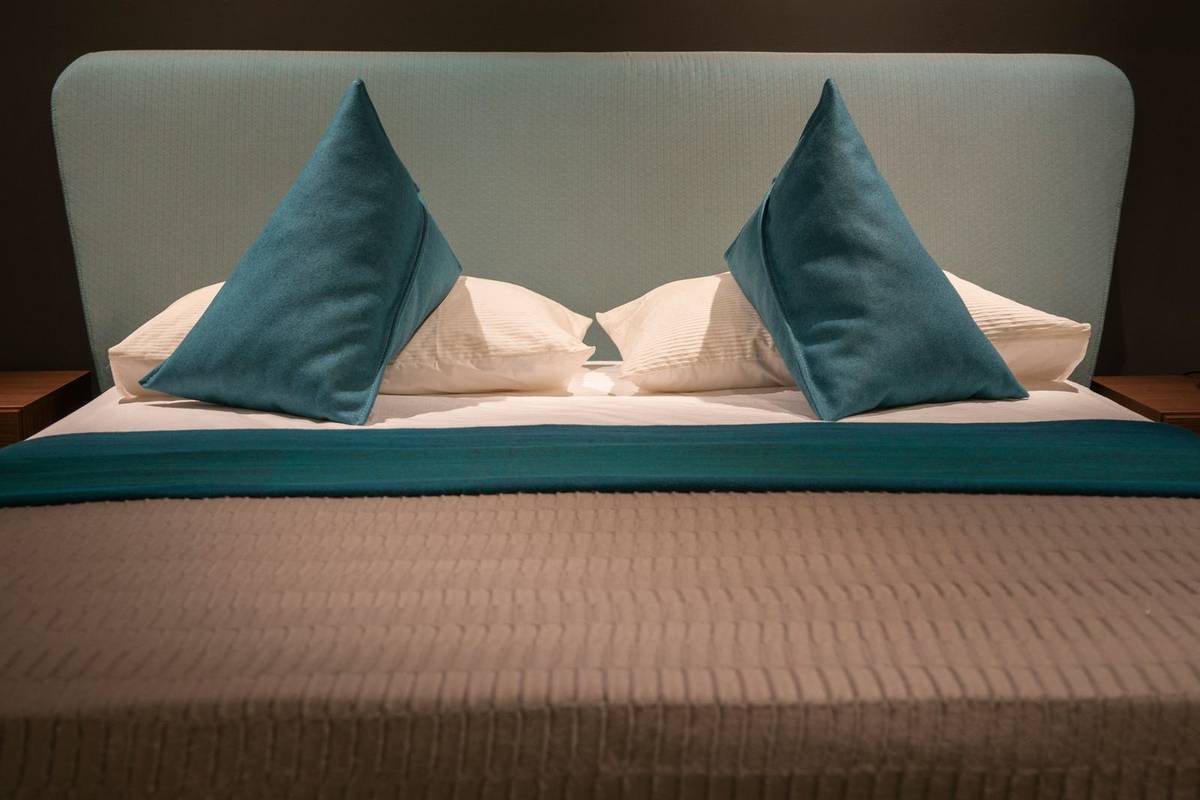 Neutral bedding with two teal accent pillows and a teal throw across the bed, under a pale aqua headboard