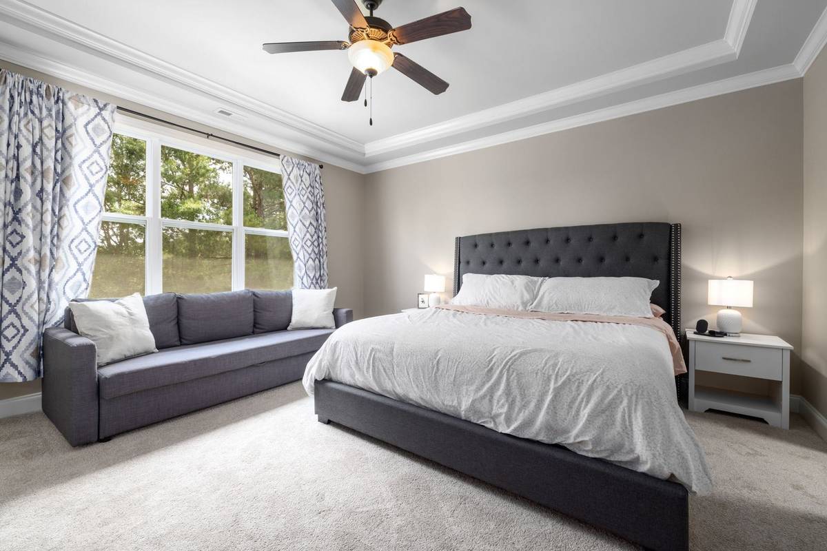 A king bed with a white comforter hanging over the sides of a gray upholstered frame, between two nightstands
