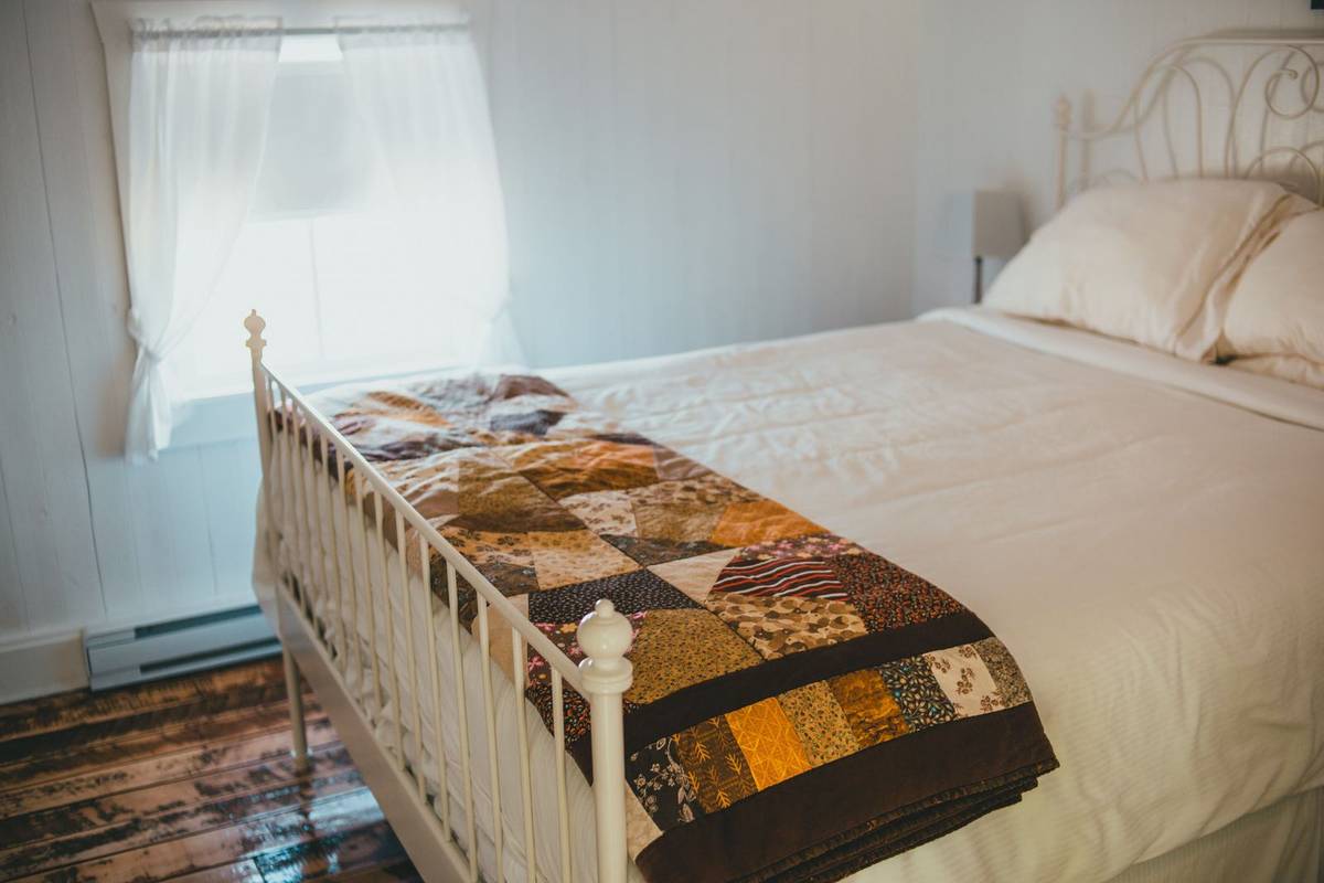 A patchwork quilt folded into a long strip across the foot of a white bed with an iron frame