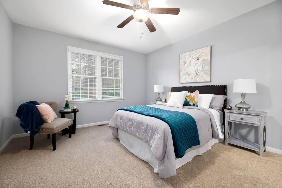 A wood ceiling fan with a light kit over a bedroom with a gray and teal bed