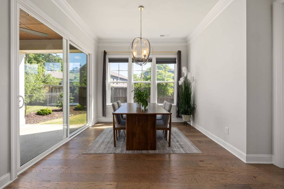 An orb chandelier hanging over a narrow wood dining table in front of a window