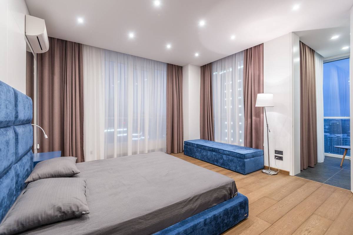 A bedroom with mauve curtains over sheers on two walls of windows, hung from the ceiling to the floor beside a low bed