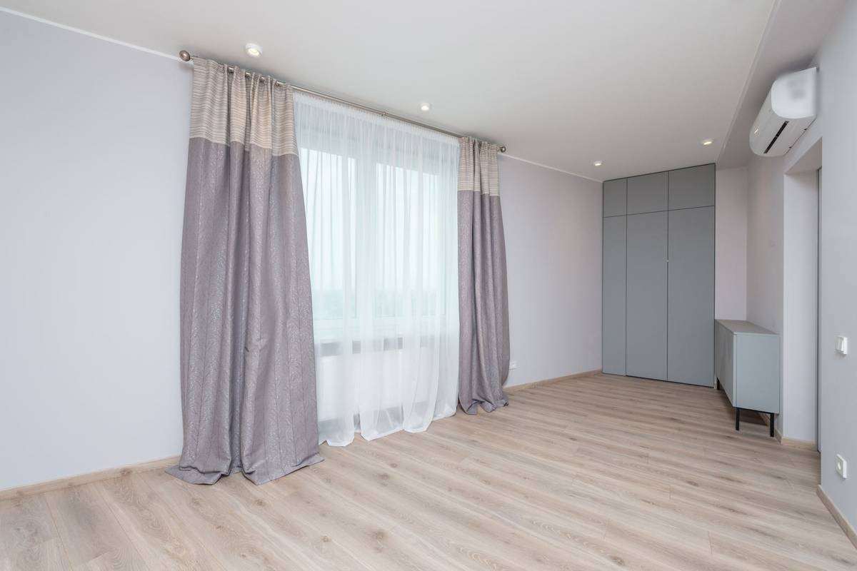 Two-tone lavender curtains and a white sheer hanging to the floor from a rod near the ceiling of an empty room