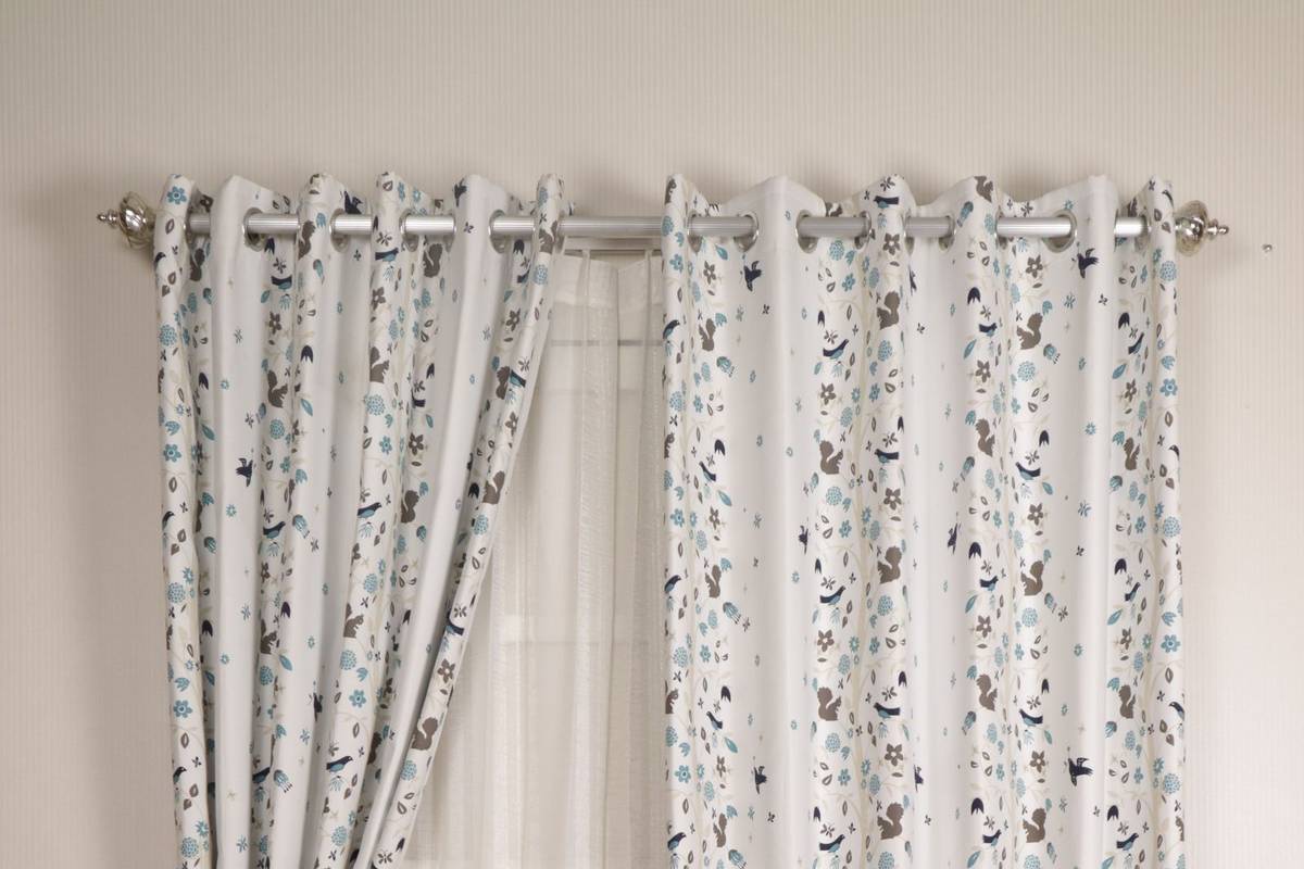 Printed grommet curtains and a white sheer hanging from a silver rod with round finials, gathered with tiebacks