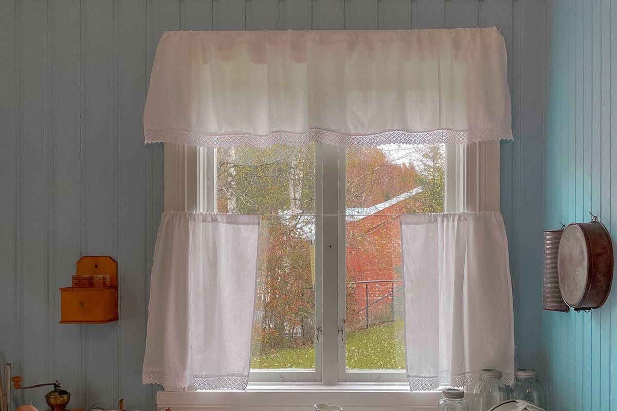 Short white cafe curtains that end at the sill, under a ruffled valance, on a kitchen window above the counter