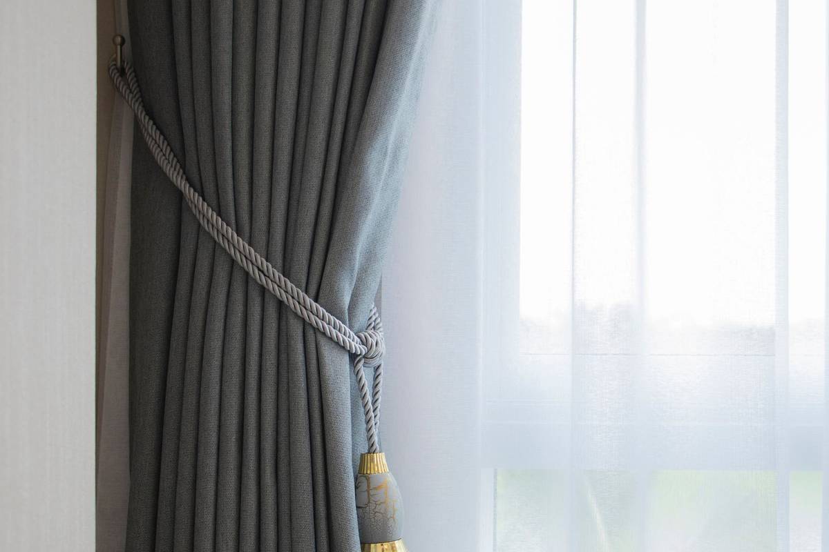 A heavy gray curtain held back with a tasseled tieback beside a white sheer that covers the window
