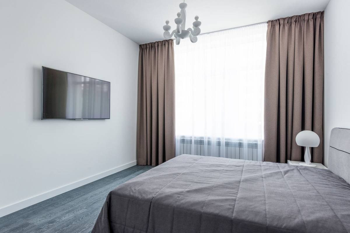Brown curtains hung near the ceiling and stacked on the wall at each side of a tall window with sheers, in a bedroom