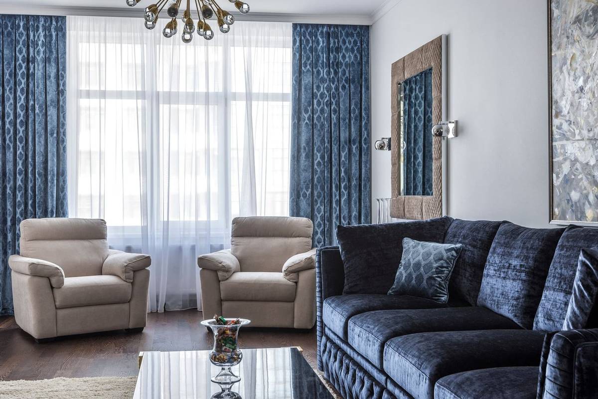 Floor-length blue drapes hung near the ceiling and wide of the window, with sheers between them, behind a velvet sofa