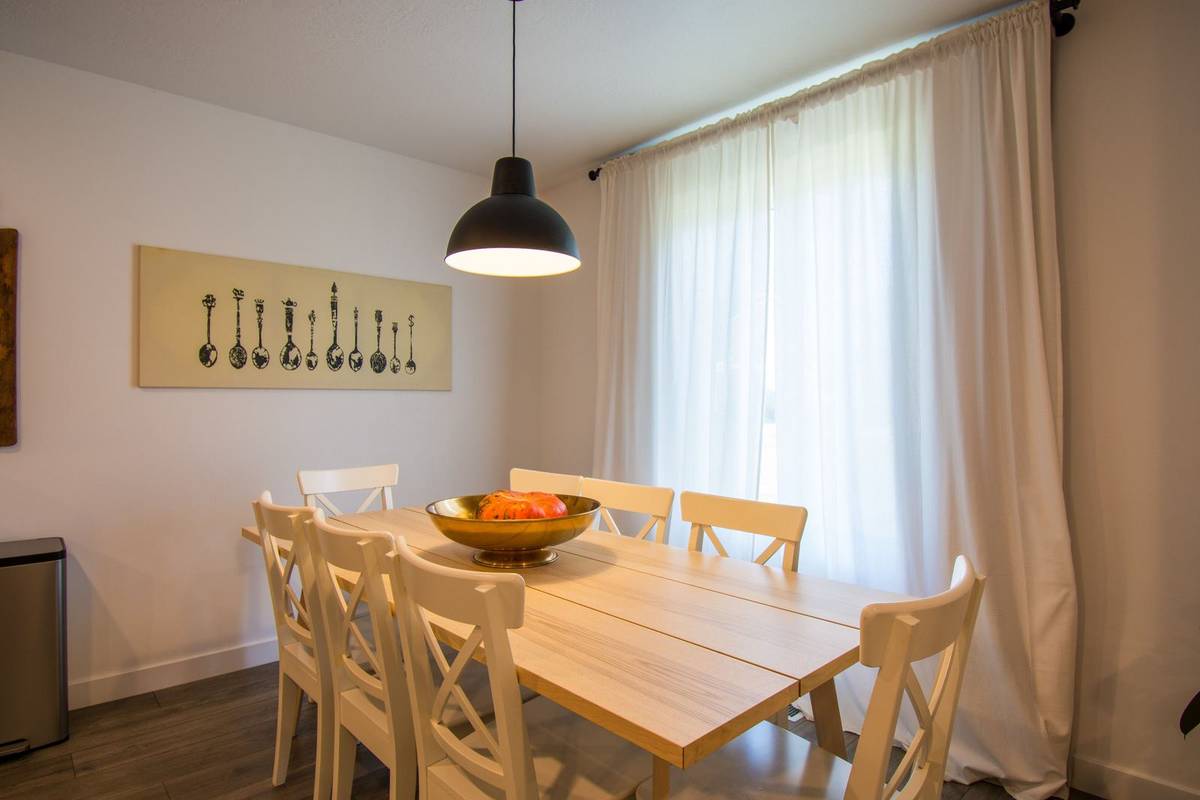 White curtains hung from a rod near the ceiling and past the window's sides, beside a pine table under a black pendant