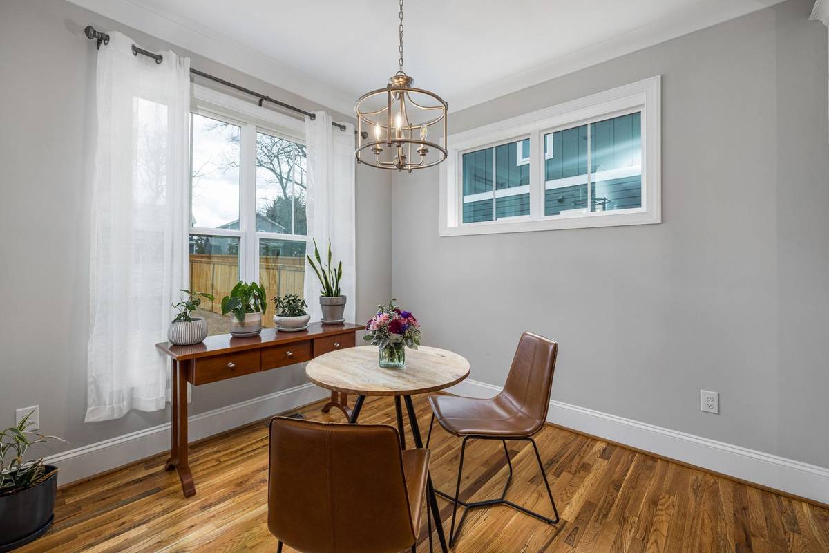 A small round wood table with two leather chairs under a lantern chandelier, beside a window with sheer curtains