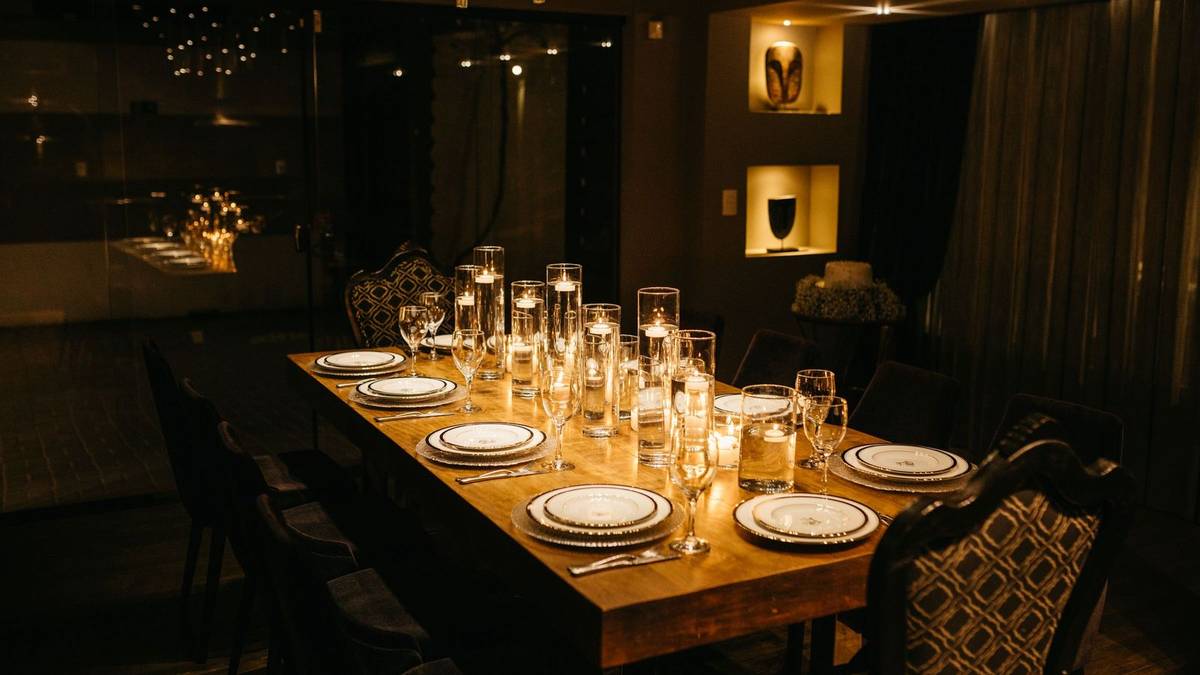 A long wood table set with plates, glasses and candles in a dim dining room