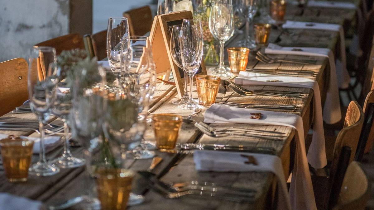 A long rustic table set with glasses and napkins down its length for a large dinner