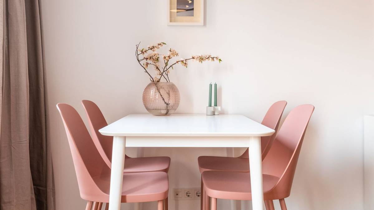 A small white dining table with four pink chairs against a light wall