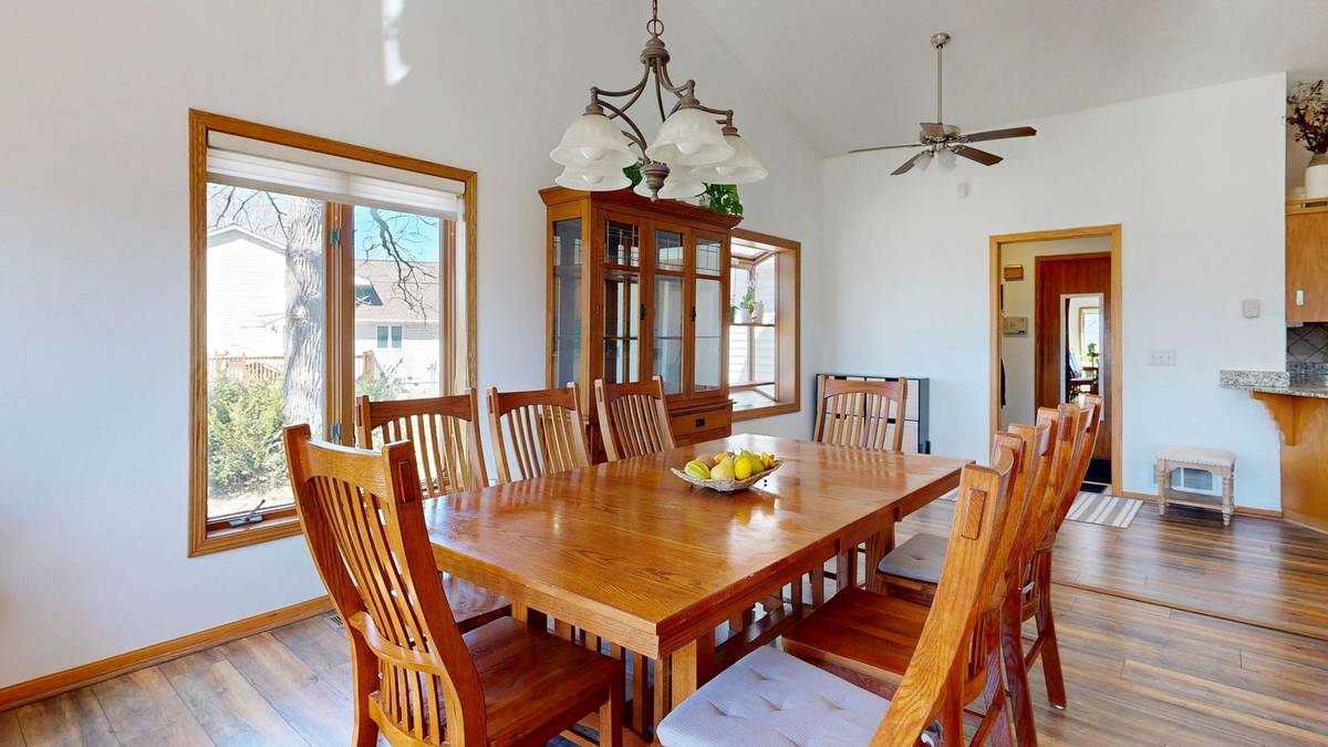 A long wood dining table ringed with slat-back chairs under a pendant light in a bright room
