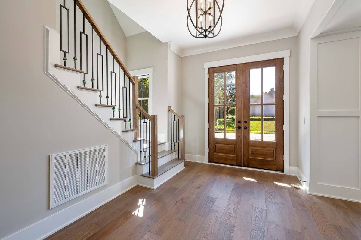 A round iron lantern pendant high in a two-story foyer with a staircase and wood double front doors