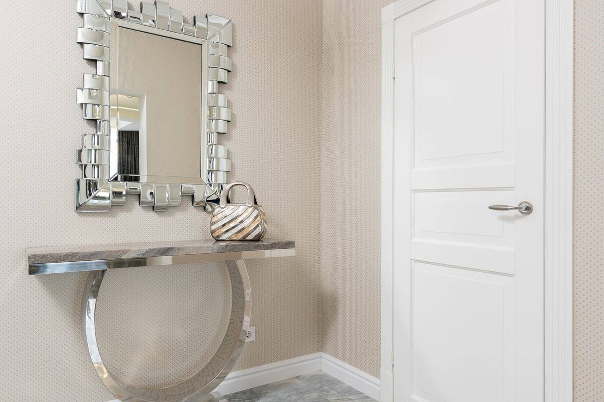 A mirror with a faceted silver frame above a shallow stone-topped console, narrower than the console below it