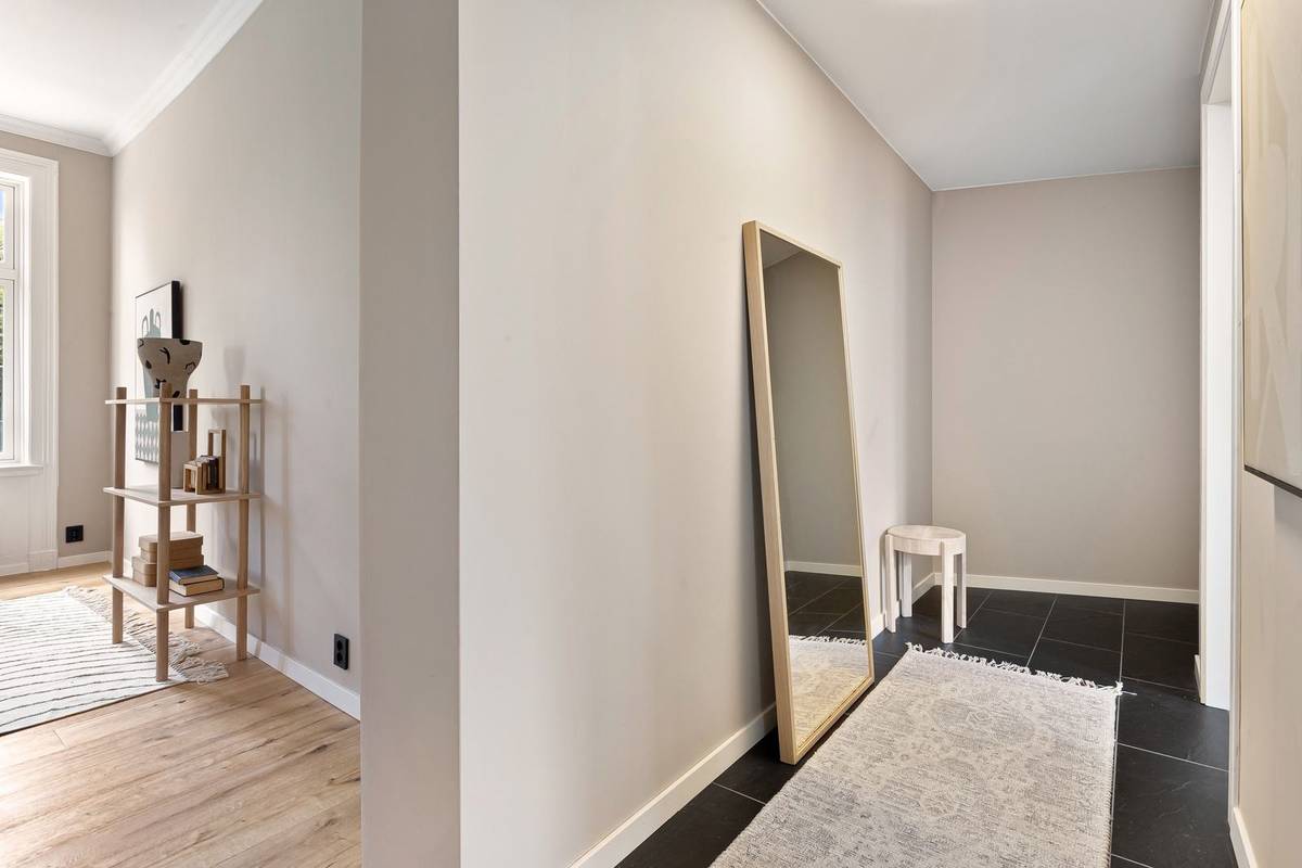 A pale runner rug down a narrow entry with dark tile, bare floor at its sides, a tall mirror leaning on the wall