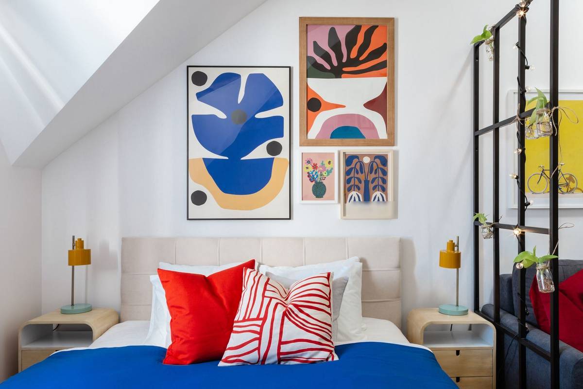 Four bold abstract prints of different sizes grouped above an upholstered headboard, between two bedside lamps