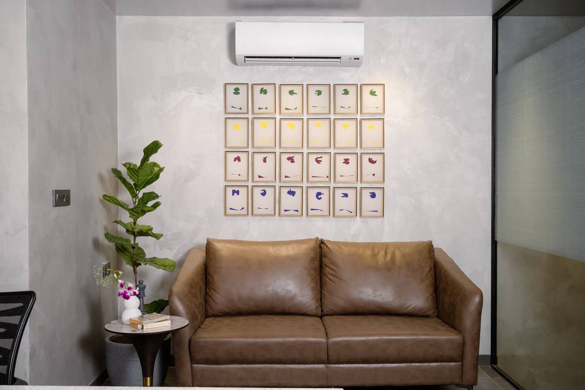 Twenty-four matching gold frames hung in an even grid of four rows above a brown leather sofa