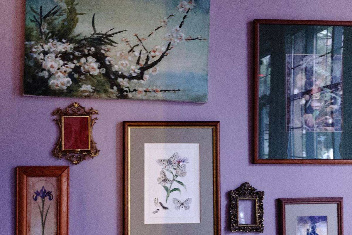 A salon wall on a lavender wall: a painting of a flowering branch, botanical prints and two small gilded frames