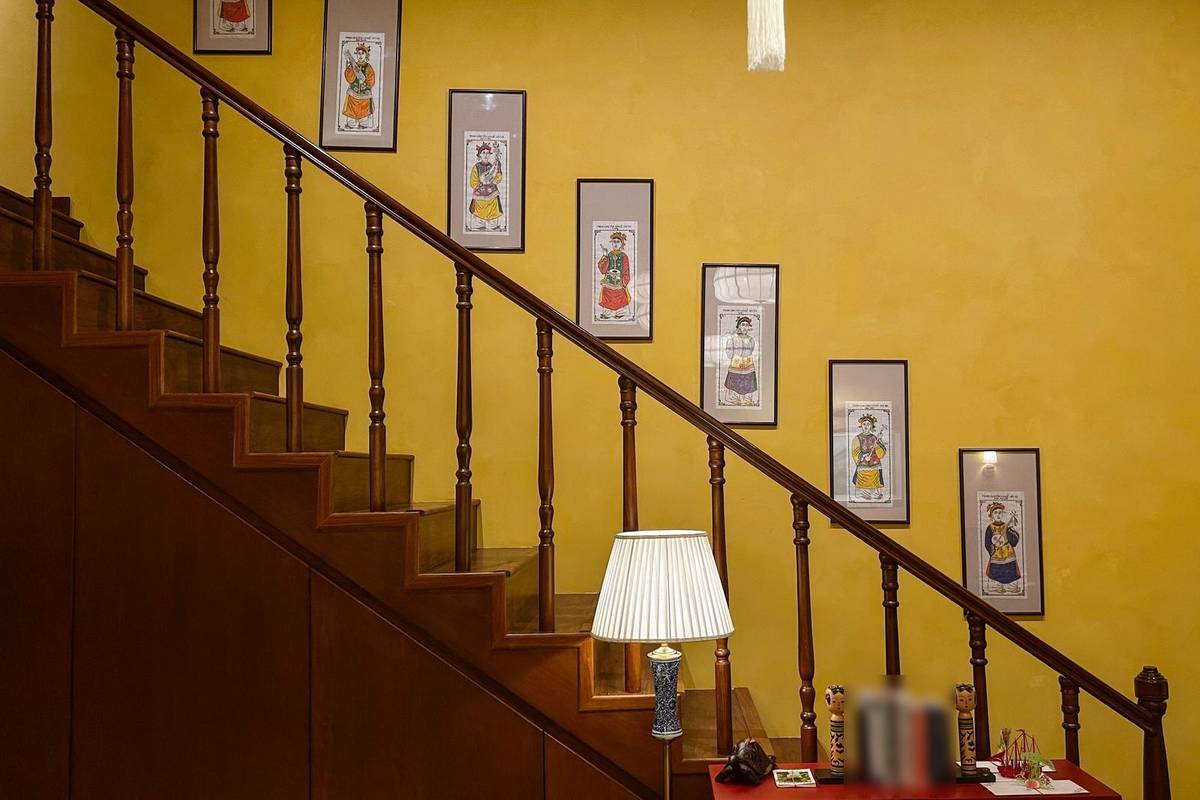 A row of matching framed prints climbing a yellow stair wall, each one a step higher, in line with the handrail