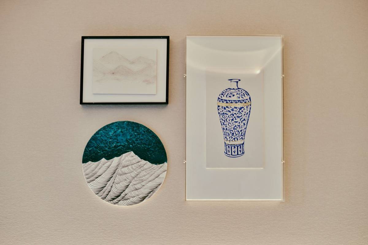 A small group of three pieces: a framed landscape drawing, a round painted panel and a tall print of a blue vase