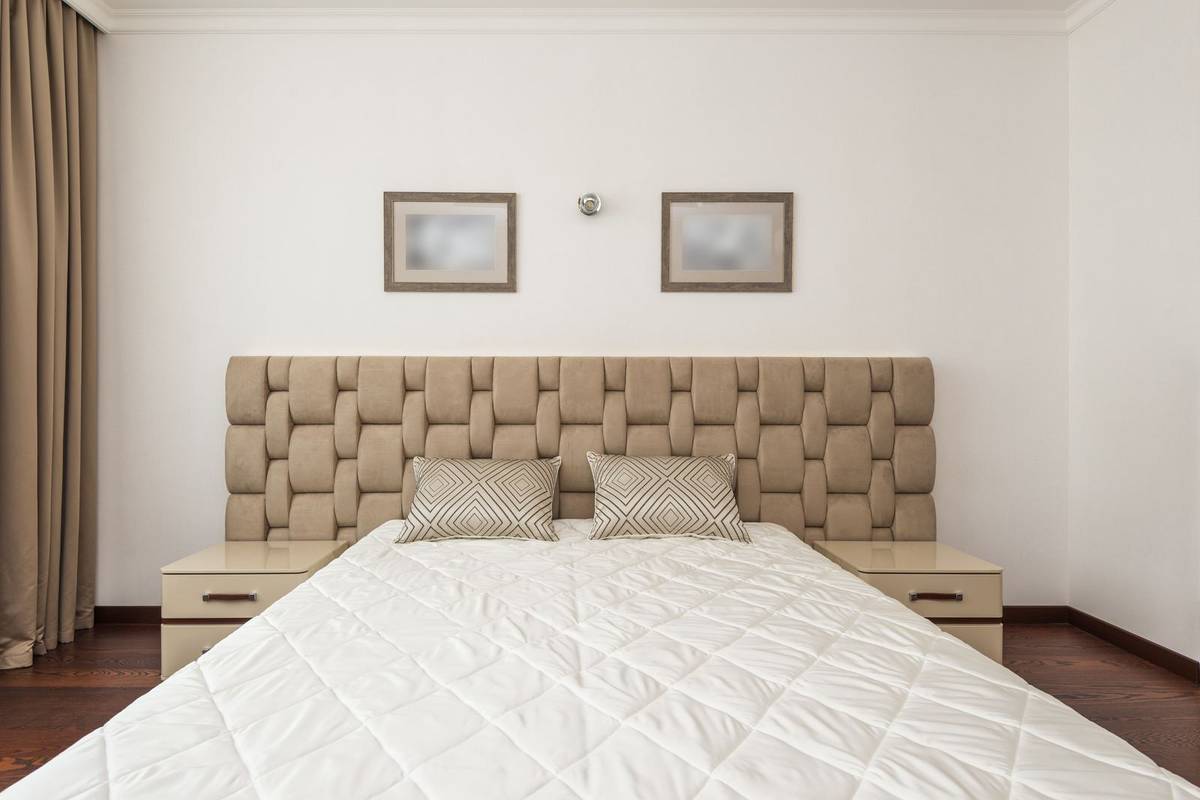 A woven upholstered headboard running past both nightstands, with two small framed pictures above the bed