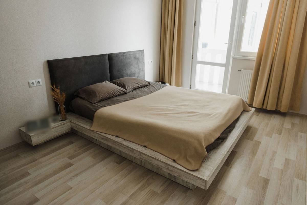 A low platform bed with two dark upholstered panels on the wall as its headboard and a floating wood nightstand