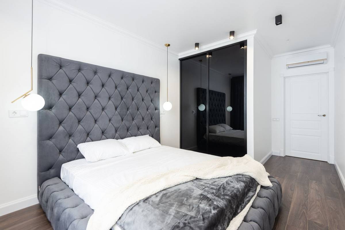 A tall gray tufted headboard rising well above the pillows, with globe pendant lights at both sides of the bed