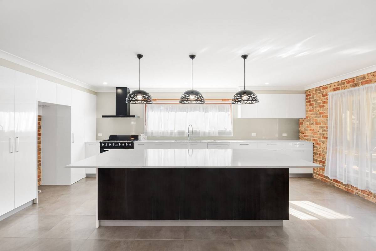 A long island with a white top and a dark base under three black dome pendants, with wide aisles all around