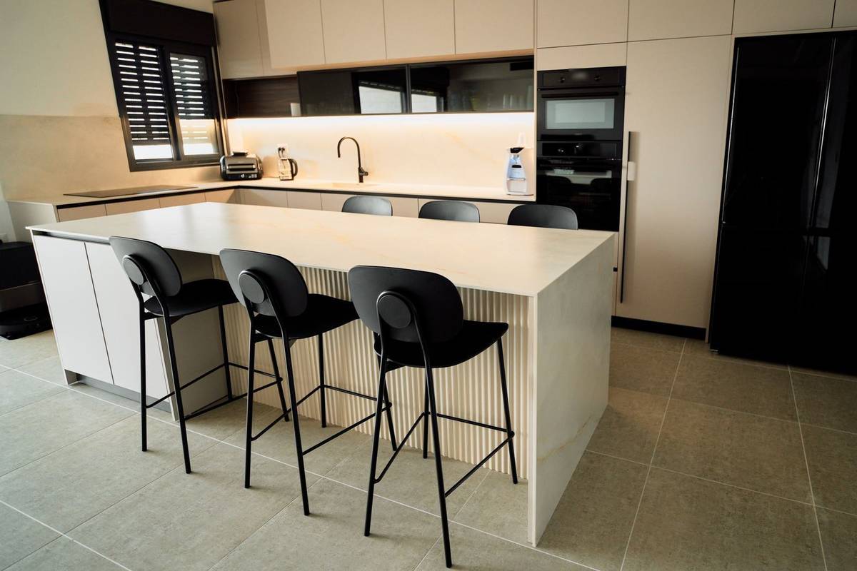 A white waterfall island with black bar stools on two sides and wide open floor behind the stools