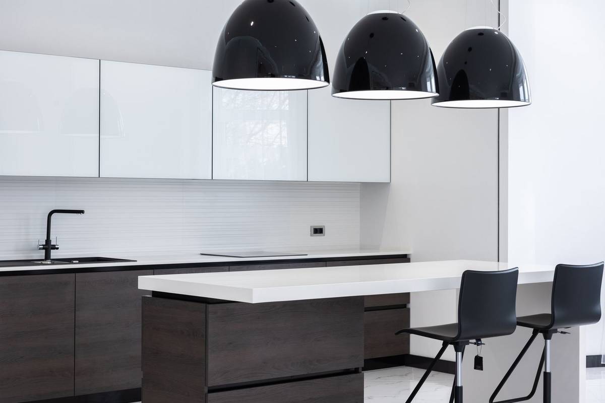 Three large black dome pendants low over a white island counter with two black bar stools