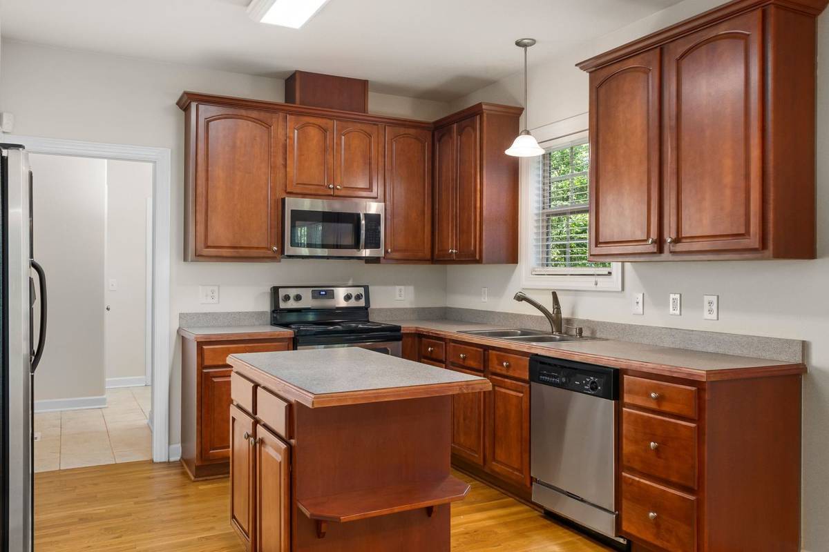A small square island with a laminate top in a compact wood kitchen, with open floor between it and the counters