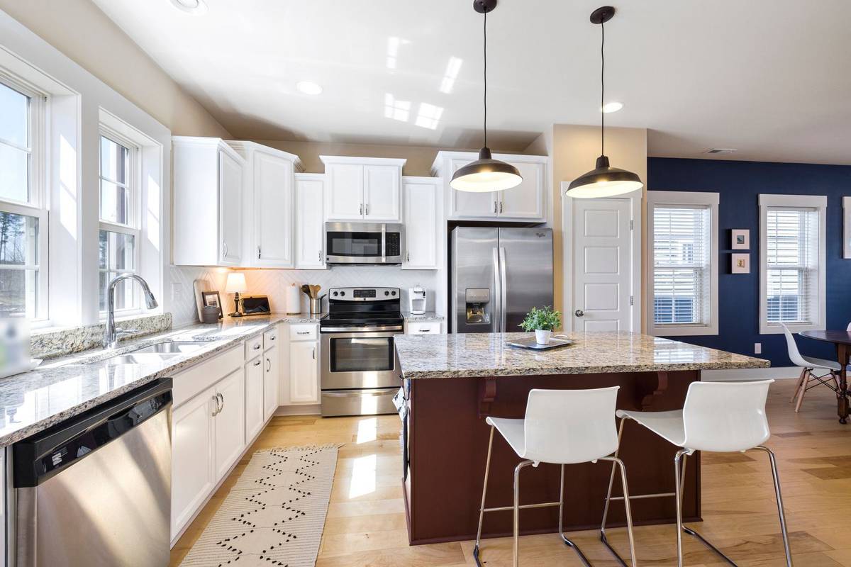 Two black pendant lights over a granite island with corbels under its overhang and two white stools