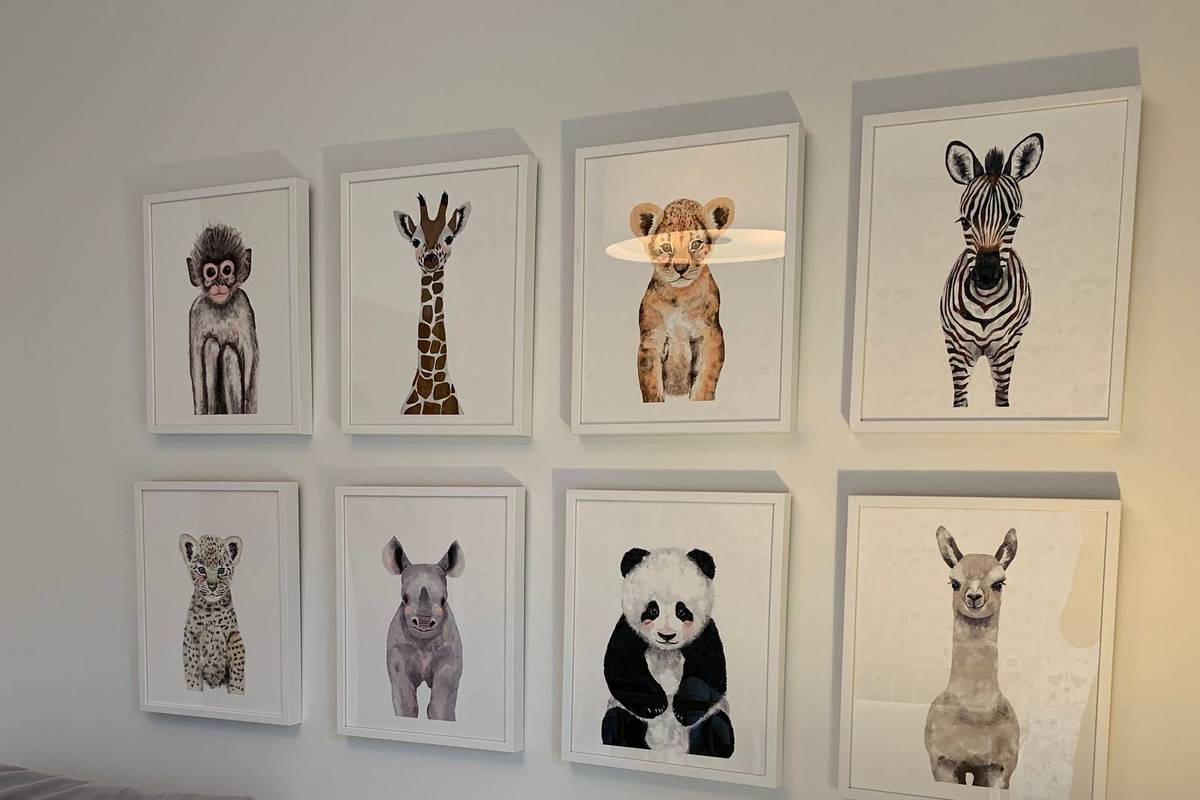 Eight framed watercolor prints of baby animals hung in an even grid of two rows on a white nursery wall
