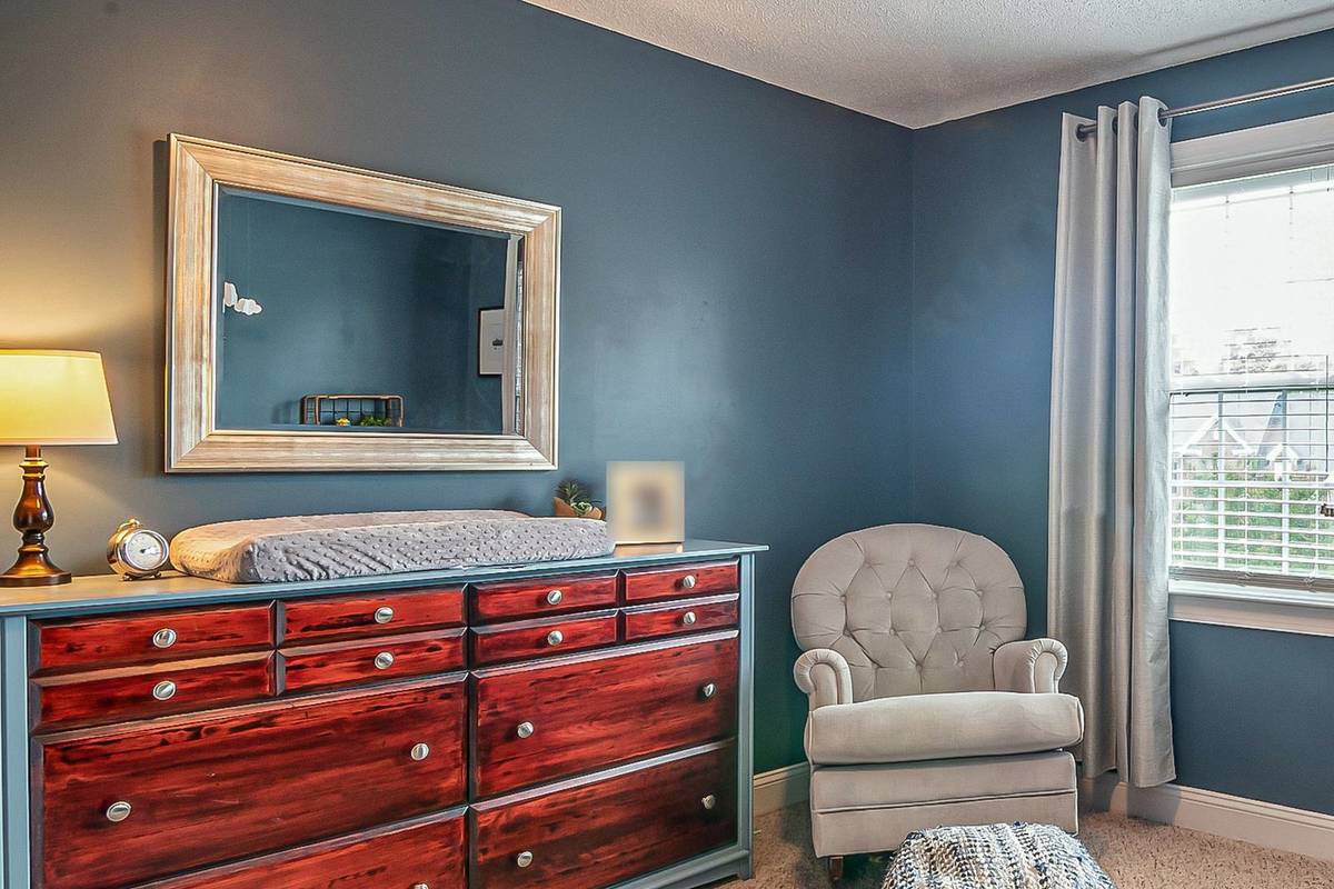 A changing pad on top of a wide wood dresser under a mirror, with a tufted glider by the window
