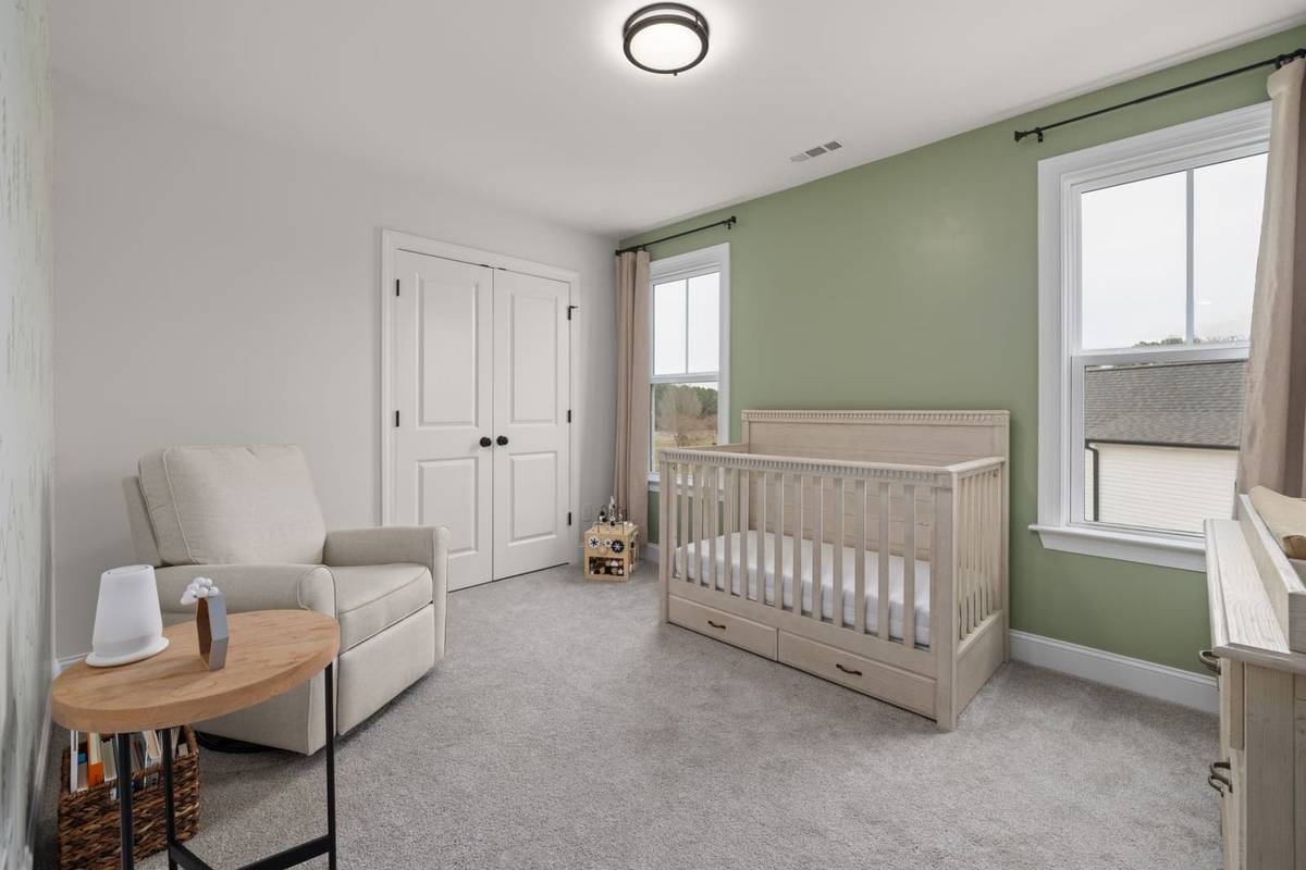 A bright nursery with a sage green wall, a whitewashed wood crib with only a fitted sheet, and a beige glider