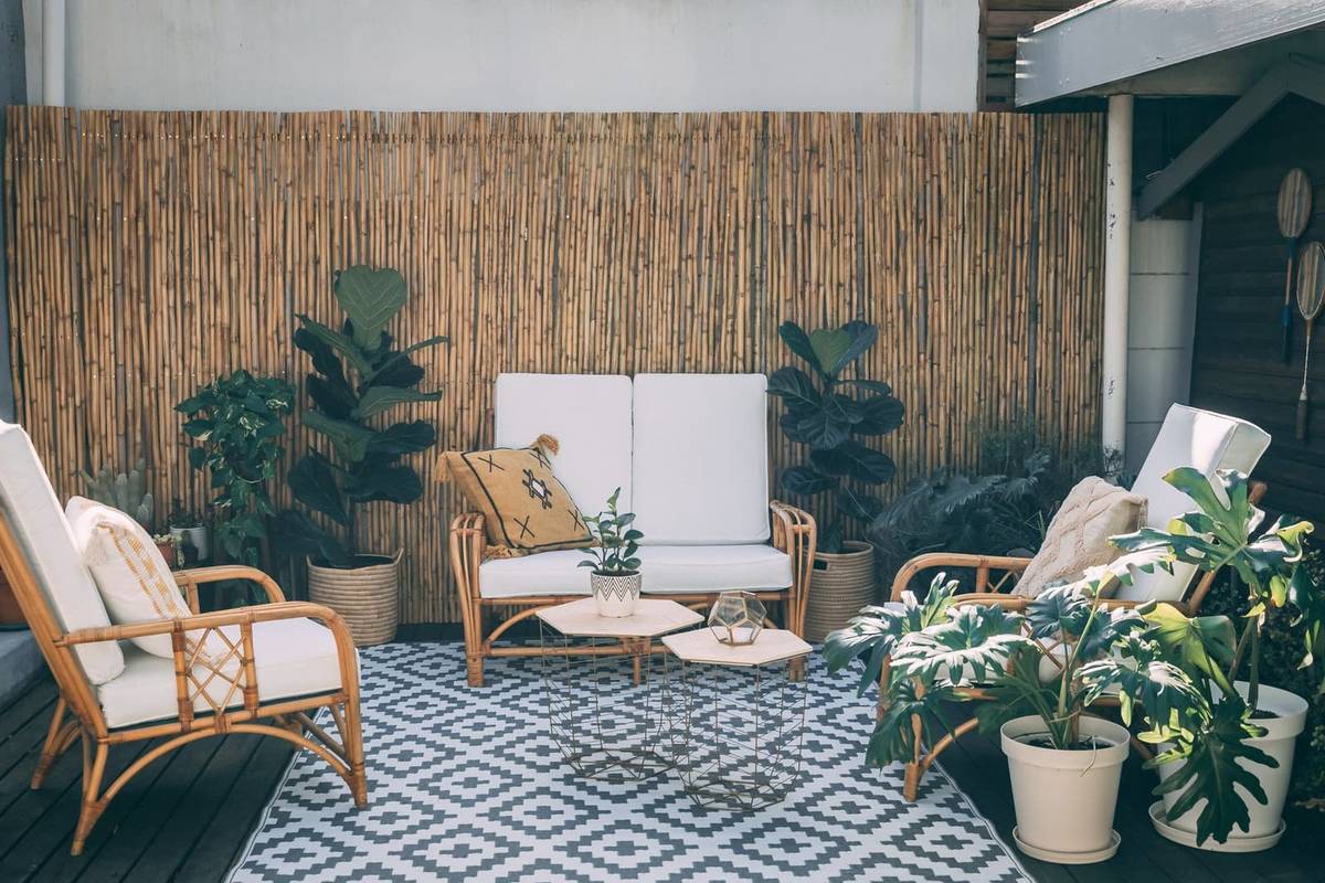 A blue and white patterned outdoor rug under a rattan loveseat and two rattan armchairs, against a bamboo screen