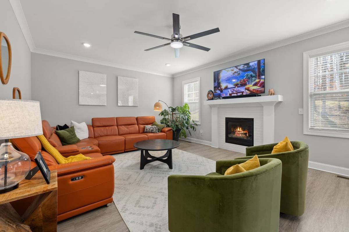 A living room with light gray walls, an orange leather sectional, two olive green velvet armchairs and a white fireplace