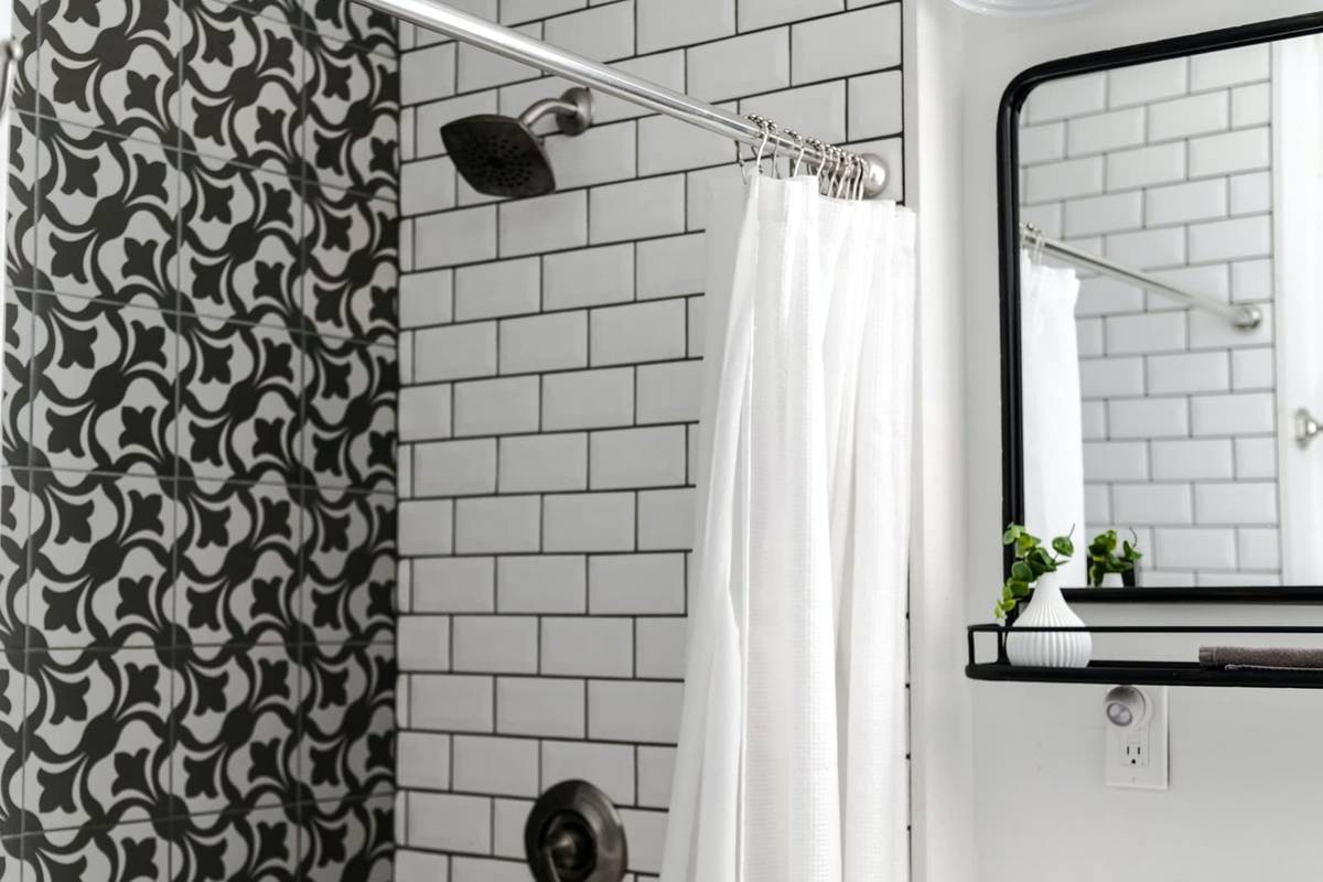 A white shower curtain on metal rings hanging from a curved rod over a bathtub, against white subway tile