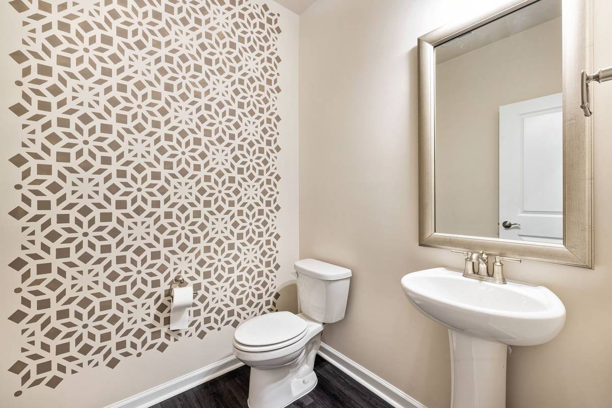 A powder room with a pedestal sink under a framed mirror, a toilet and a stenciled pattern on the wall behind it