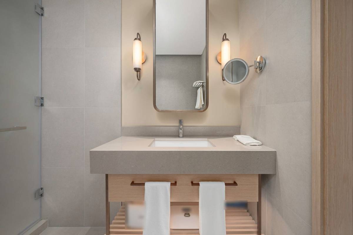 A vanity with a tall mirror between two wall sconces, towels on the drawer pulls and a slatted shelf below