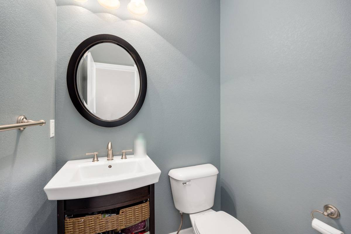 A half bath with a small sink on an open stand, a storage basket below, a round mirror and the toilet beside it