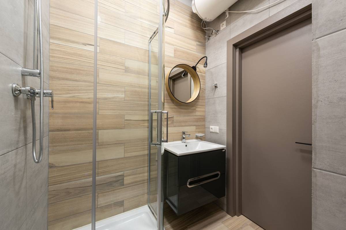 A small bathroom with a glass shower stall, a wall-hung vanity with drawers and a round mirror beside the door