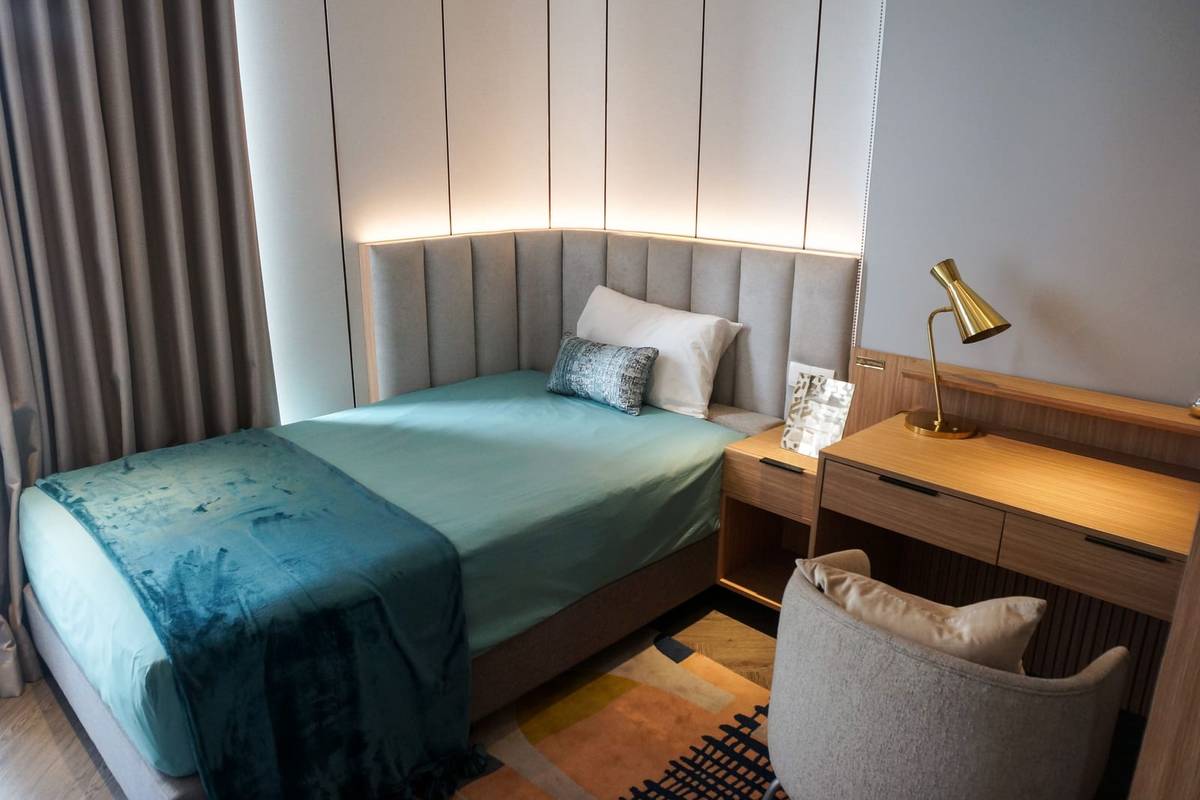 A single bed with an upholstered headboard beside a wood desk, a desk lamp and a gray armchair