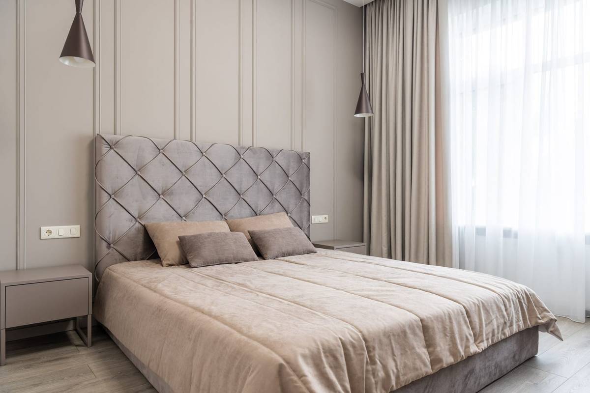 A tall tufted headboard on a paneled wall, pendant lights at each side of the bed and curtains hung from near the ceiling