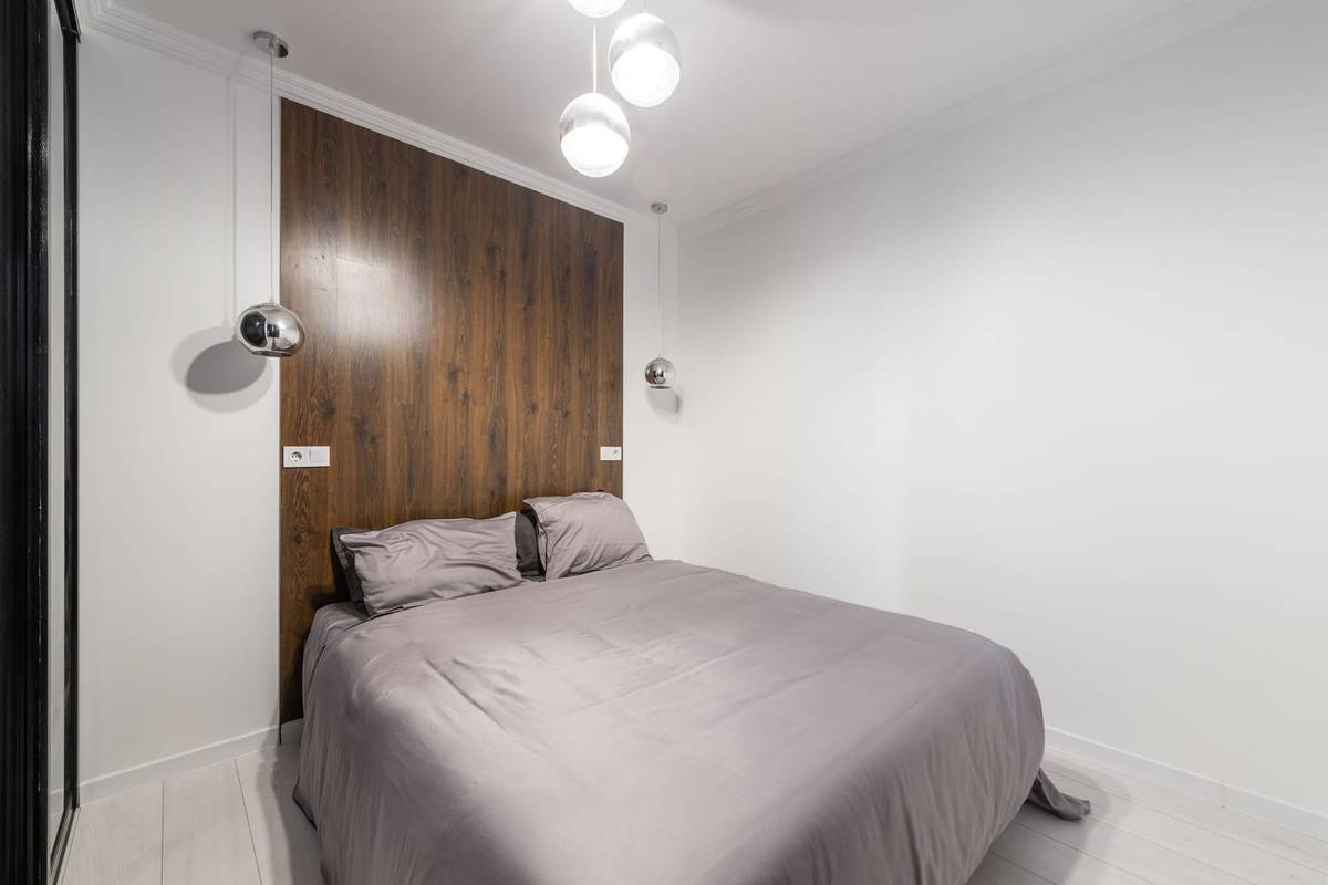Glass pendant lights hanging at both sides of a bed set against a dark wood wall panel, with no nightstands